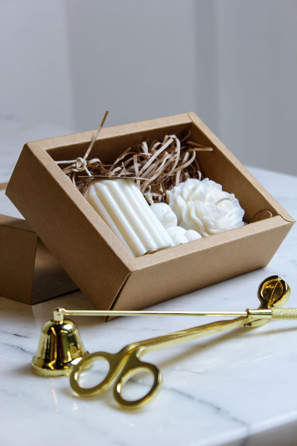 Coffret cadeau en carton kraft contenant des bougies parfumées, posé sur du marbre clair avec un éteignoir doré
