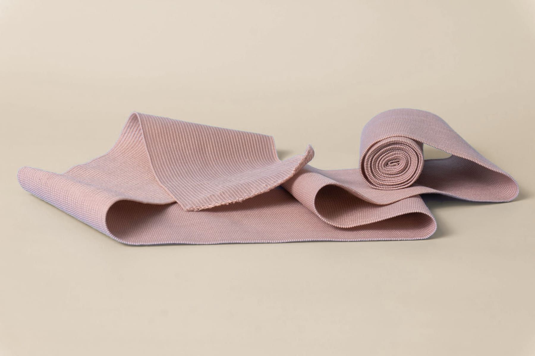 Bande de contention élastique couleur chair, roulée et déroulée sur un fond sable clair