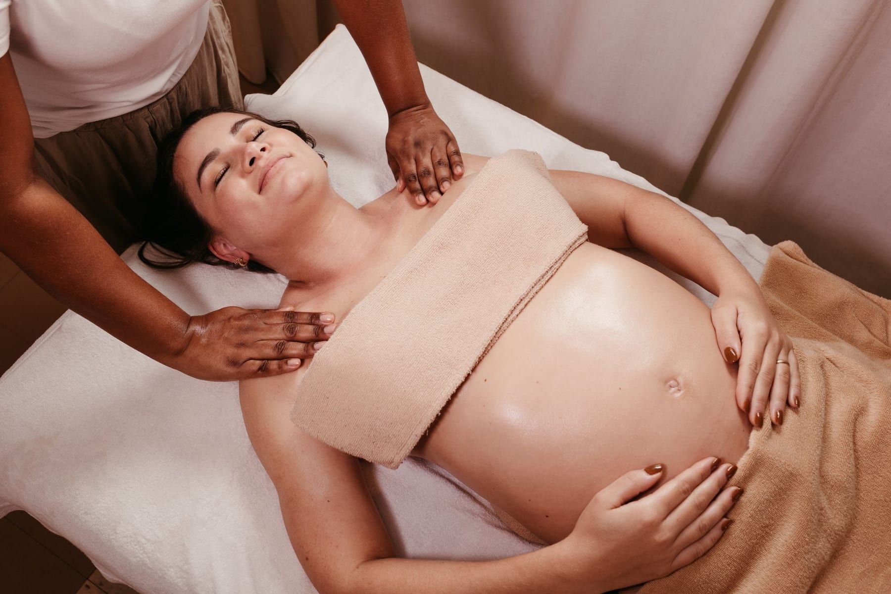 Femme enceinte allongée et détendue pendant un massage des épaules, dans une pièce calme aux tons doux