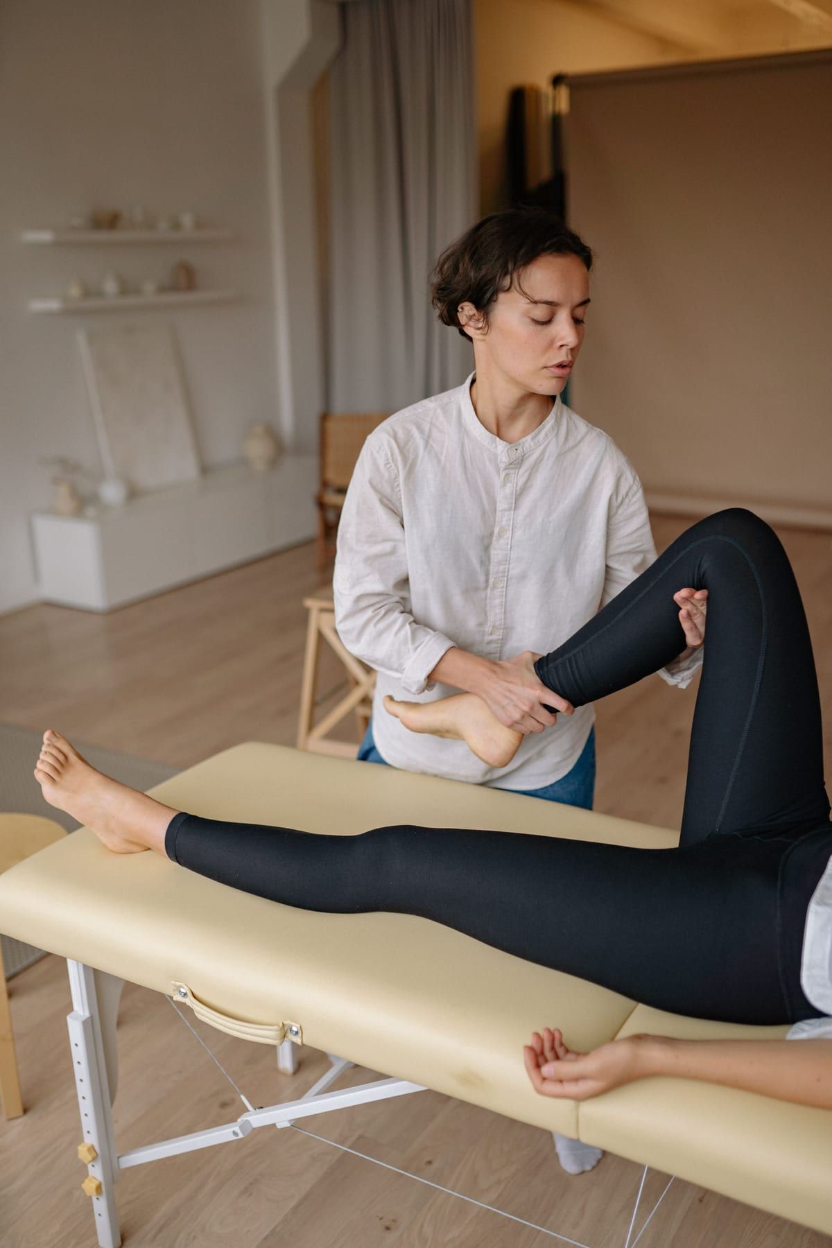 Thérapeute mobilisant la jambe d’une personne allongée sur une table de massage, dans une pièce claire aux tons naturels