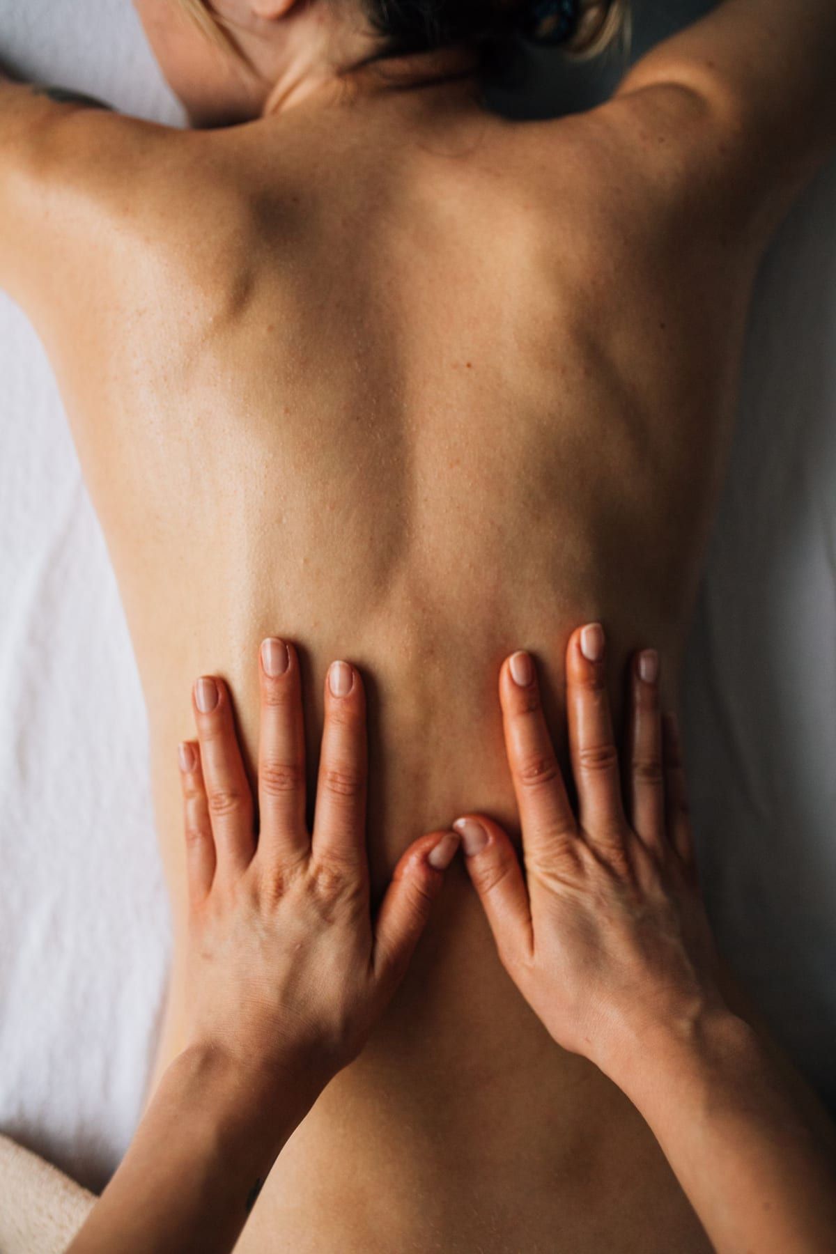 Les deux mains d’un thérapeute posées sur le bas du dos d’une personne allongée sur une table de massage, lumière douce